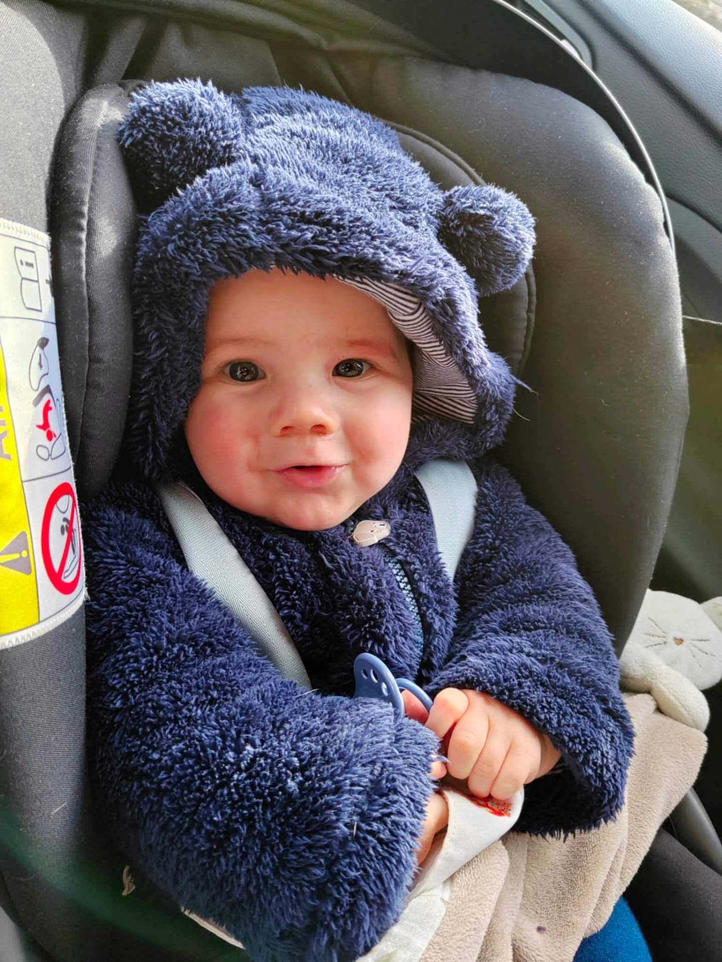 Maël a rejoint le concours — aidez-le/la à gagner de superbes lots ! baby, child, car_seat, hoodie, blue_clothing, pacifier, infant, cute, smiling, face, hands, seatbelt, plush, warm_clothing, indoor, portrait, person, cozy, car, sitting