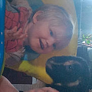 Axel is registered to the contest to win money with this photo: toddler, child, puppy, dog, pet, indoor, smiling, happy, person, young_child, animal, playing, face, hand, clothing, yellow_chair, home, cute, interaction, light