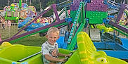 Jacob is registered to the contest to win money with this photo: child, boy, amusement_ride, dinosaur, fairground, outdoor, daylight, smile, green, colorful, ride, fun, people, grass, trees, summer, happiness, entertainment, festival, playful