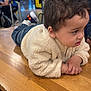 toddler, child, indoor, table, wood, curly_hair, jacket, cream_color, people, background, signs, casual_clothing, floor, seating, waiting_area, curious, hands, shoes, jeans, public_space