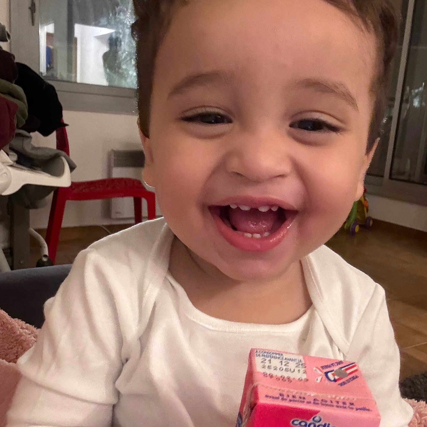 Othman a rejoint le concours — aidez-le/la à gagner de superbes lots ! blanket, child, cozy, curly_hair, face, floor, furniture, hands, happy, home, indoor, juice_box, laughing, person, smiling, toddler, toy, white_clothing, window, young_child