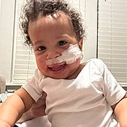 Xavier is registered to the contest to win money with this photo: baby, child, curly_hair, medical_tape, white_onesie, smiling, indoor, window_blinds, happy, person, face, infant, cute, holding_hand, skin, young_child, portrait, bright, healthcare, toddler