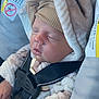 baby, sleeping, car_seat, infant, child, hat, blanket, safety_harness, warning_label, cozy, cute, face, clothing, car_interior, seatbelt, peaceful, resting, young_child, soft_texture, bundle