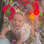 Scarlet is registered to the contest to win money with this photo: baby, baby_clothing, blanket, camera_facing, child, colorful, floral_pattern, happy, indoors, infant, nursery, play_area, playmat, plush_toy, portrait, rattles, sitting, smiling, stacking_cups, toys