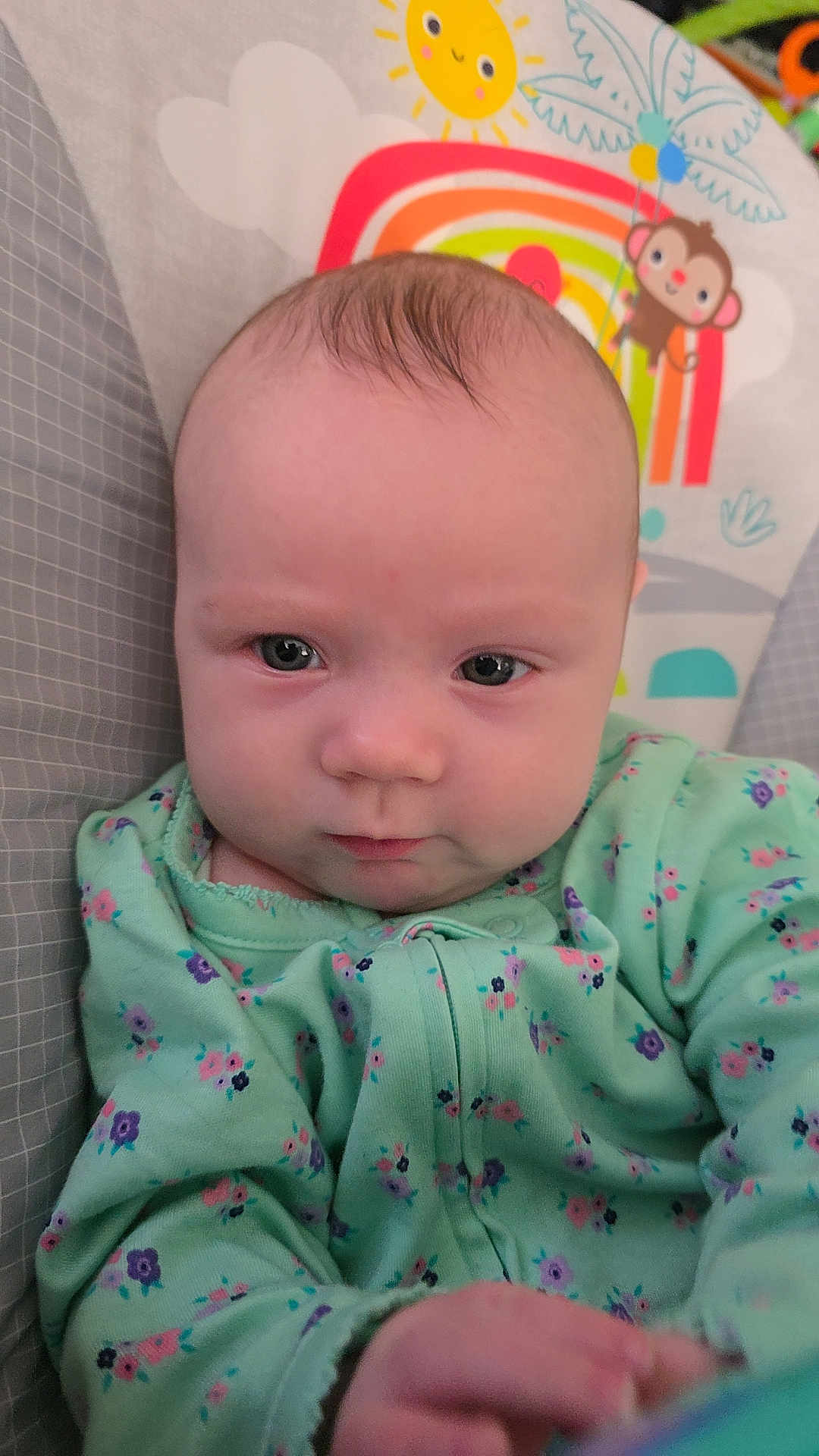 Scarlet is registered to the contest to win money with this photo: baby, infant, child, onesie, floral_pattern, face, eyes, hair, baby_chair, rainbow, sun, monkey, toy, colorful, cute, portrait, indoor, expression, closeup, person