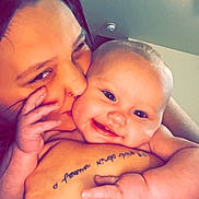 Ella Mae Graham is registered to the contest to win money with this photo: baby, smiling, adult, kiss, close_up, hand, face, skin, tattoo, indoor, person, affection, love, cheek, happy, infant, cuddling, human, portrait, warmth
