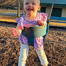 child, toddler, swing, playground, outdoor, barefoot, purple_clothing, trees, sunlight, smiling, fun, play, metal_chains, woodchips, park, daylight, blurry_face, happy, person, recreation