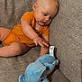 baby, infant, child, orange_onesie, plush_toy, blue_elephant, couch, sofa, furniture, indoor, curious, reaching, soft_toy, cute, young_child, toddler, relaxed, home, fabric, playtime