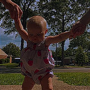 Ella Mae Graham is registered to the contest to win money with this photo: baby, child, toddler, walking, holding_hands, romper, strawberry_pattern, outdoor, sidewalk, trees, grass, suburban, daylight, barefoot, person, support, summer, young_child, sky, nature