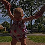 baby, child, toddler, walking, holding_hands, romper, strawberry_pattern, outdoor, sidewalk, trees, grass, suburban, daylight, barefoot, person, support, summer, young_child, sky, nature