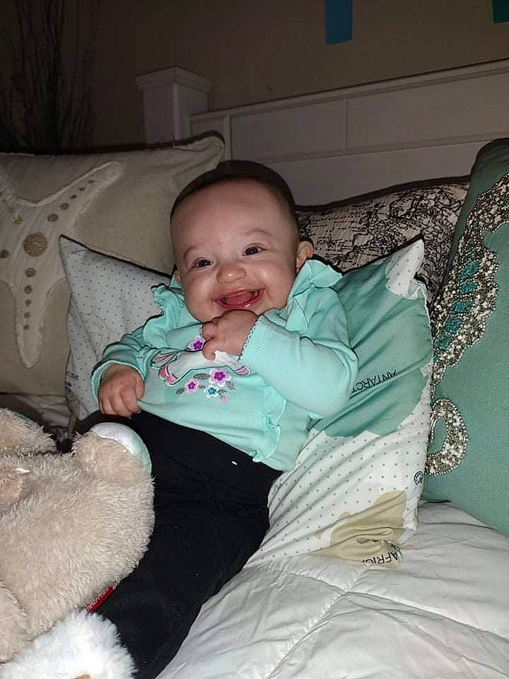 Raelynn is registered to the contest to win money with this photo: baby, baby_toddler_clothing, cheek, child, comfort, couch, event, eye, happy, head, human_body, iris, lap, linens, person, room, sitting, skin, smile, textile