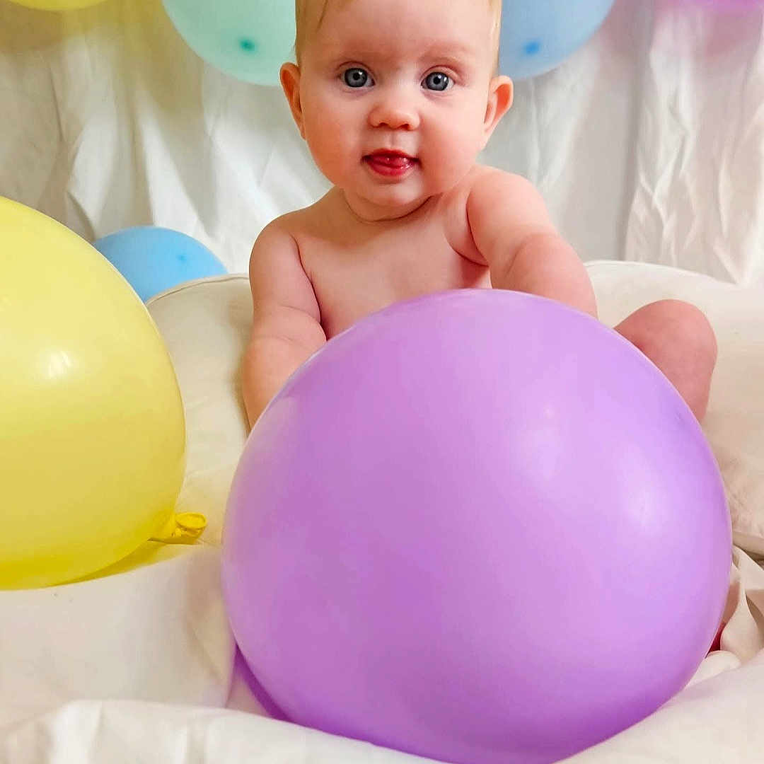 Lyla is registered to the contest to win money with this photo: baby, balloon, blue_eyes, child, cute, face, indoors, infant, light_skin, looking_at_camera, pastel_colors, playful, portrait, round_cheeks, sitting, soft_lighting, tongue_out, white_background, yellow_balloon, young_child