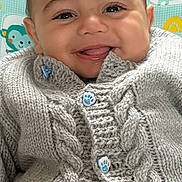 Flynn is registered to the contest to win money with this photo: baby, smiling, face, knitted_sweater, button, paw_print, high_chair, animal_pattern, cute, child, indoor, portrait, happy, clothing, infant, closeup, seated, warm, cozy, playful