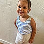 toddler, child, smiling, braided_hair, beads, striped_tank_top, knitted_shorts, standing, indoor, textured_wall, happy, cute, person, portrait, young_child, floor, skin, arm, face, fashion