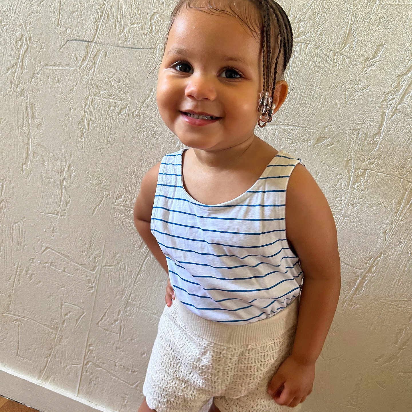 Bryhana participe au concours pour gagner de l'argent avec cette photo : arm, beads, braided_hair, child, cute, face, fashion, floor, happy, indoor, knitted_shorts, person, portrait, skin, smiling, standing, striped_tank_top, textured_wall, toddler, young_child