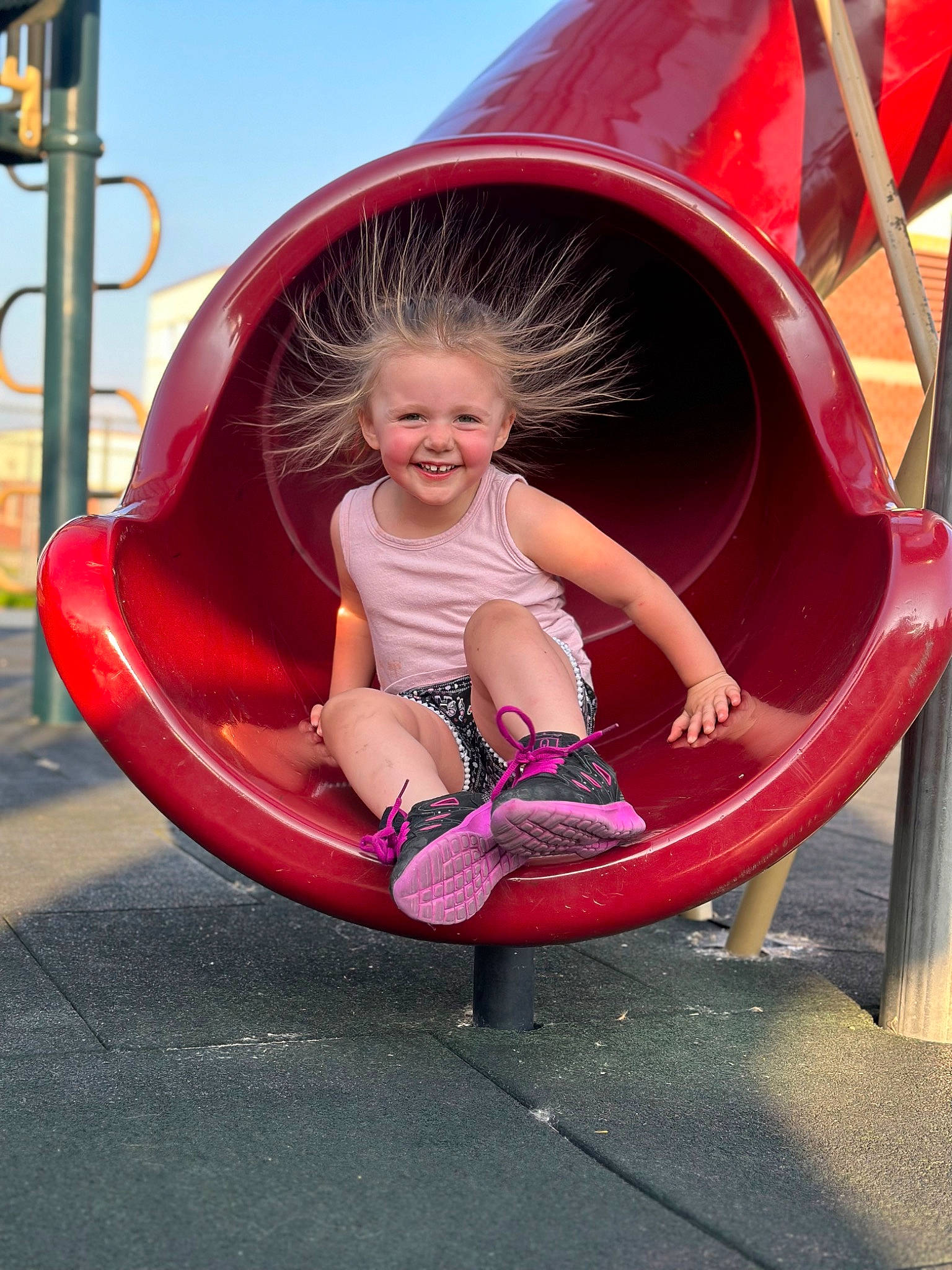 Harlee is registered to the contest to win money with this photo: automotive_tire, baby_toddler_clothing, bumper, child, chute, city, facial_expression, fun, joy, leg, leisure, magenta, outdoor_play_equipment, person, pink, playground, playground_slide, recreation, red, sky