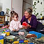 Kena a rejoint le concours — aidez-le/la à gagner de superbes lots ! child, adult, indoor, toys, blanket, glasses, woman, playing, floor, sitting, sneakers, bookshelf, plants, door, smile, interaction, colorful, home, family, engagement