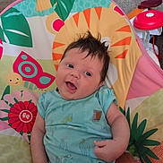 Lillian joined the competition — help win amazing prizes! baby, child, infant, smiling, happy, portrait, sitting, activity_seat, playmat, toy, rocket_toy, colorful, indoor, home, carpet, onesie, blue_clothing, dark_hair, playtime, closeup