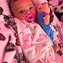 Gia joined the competition — help win amazing prizes! baby, infant, pacifier, plush_doll, blanket, onesie, dinosaur_print, pink, soft_texture, sleepwear, child, cute, cozy, lying_down, indoor, portrait, young_child, face, hand, comfort