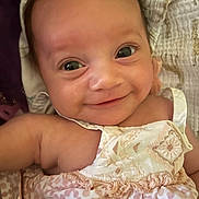 Gia joined the competition — help win amazing prizes! baby, smiling, closeup, infant, face, eyes, dress, blanket, happy, cute, child, skin, portrait, newborn, adorable, person, clothing, sleepwear, lying_down, young