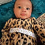 baby, infant, face, eyes, leopard_print, clothing, blanket, fabric, pattern, pout, cute, portrait, young_child, indoors, soft_texture, head, person, lying_down, colorful, warm_clothing