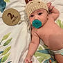 baby, infant, pacifier, knitted_hat, blanket, wooden_sign, 2_months, cute, lying_down, raised_fist, soft_texture, patterned_blanket, milestone, adorable, child, headwear, celebration, indoor, portrait, young
