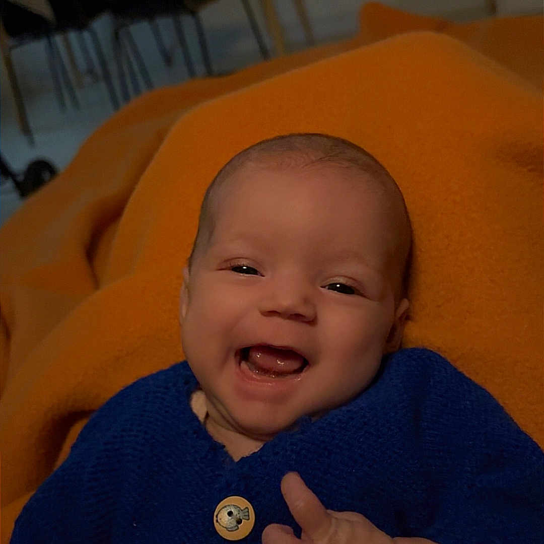 Maïwayne a rejoint le concours — aidez-le/la à gagner de superbes lots ! baby, blue_sweater, button, chair, clothing, cozy, cute, dining_area, face, furniture, hand, happy, indoor, infant, orange_blanket, person, portrait, skin, smiling, table