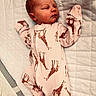 baby, newborn, sleeping, onesie, giraffe_print, pink_clothing, blanket, quilt, infant, child, cute, peaceful, resting, indoors, portrait, soft_lighting, cozy, face, head, small_person