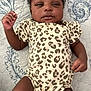 Jazaria is registered to the contest to win money with this photo: baby, infant, child, leopard_print, onesie, lying_down, blanket, pattern, curly_hair, skin, face, hands, legs, indoors, portrait, cute, calm, young, resting, clothing