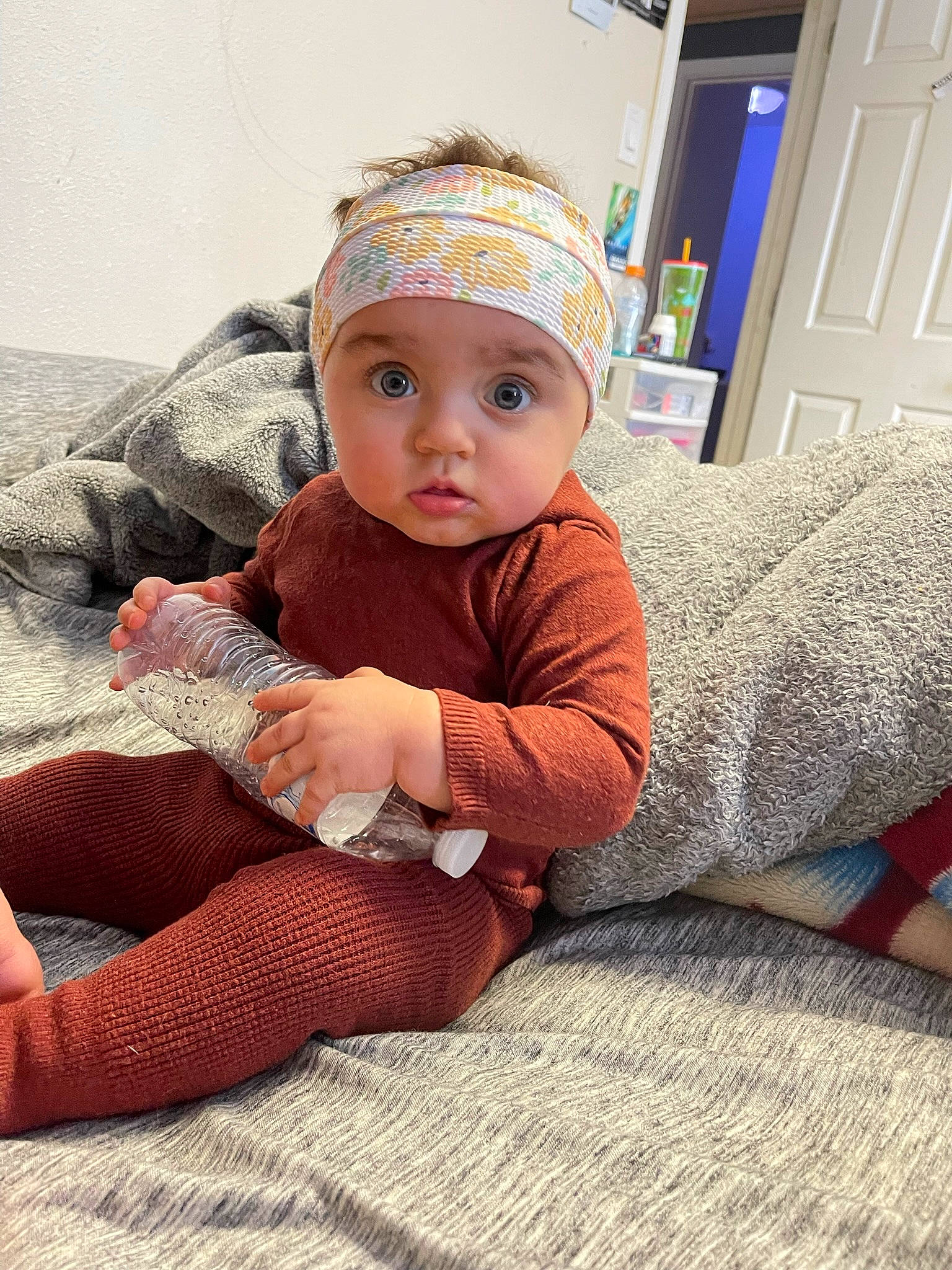 Juniper is registered to the contest to win money with this photo: baby, baby_toddler_clothing, cap, child, comfort, door, floor, flooring, foot, headwear, human_leg, knee, leg, pattern, person, sitting, skin, sleeve, sock, surprise