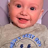 Rowan is registered to the contest to win money with this photo: baby, infant, smile, face, clothing, shirt, text, drool, happy, child, cute, portrait, seated, closeup, blue, gray, eyes, skin, head, background