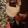cat, black_cat, christmas_stocking, holiday_decor, white_fur, tattooed_arm, indoor, christmas_tree, lights, festive, cozy, hand, animal, pet, decorations, background_blur, warm_lighting, fur, celebration, text_on_stocking
