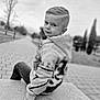 child, boy, portrait, black_and_white, outdoor, park, casual, concrete, pavement, tree, nature, young, curious, hairstyle, sitting, clothing, jacket, jeans, face, expression