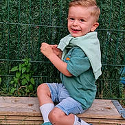 Tayler participe au concours pour gagner de l'argent avec cette photo : child, boy, smiling, outdoor, grass, wood, fence, greenery, casual_clothing, sneakers, shorts, socks, happy, portrait, sitting, daylight, haircut, playful, nature, young