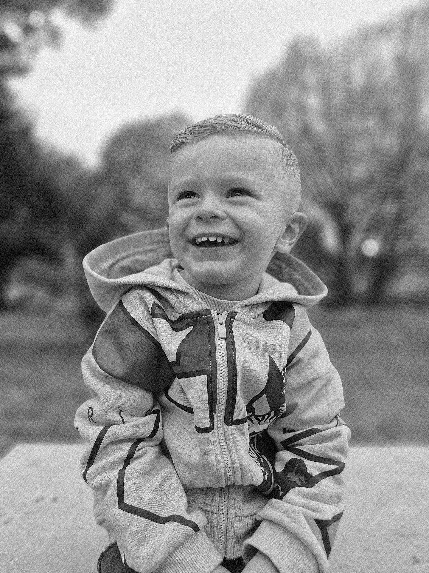 Tayler participe au concours pour gagner de l'argent avec cette photo : child, boy, smiling, hoodie, outdoor, portrait, happy, sitting, casual_clothing, young, haircut, black_and_white, cute, youth, joyful, face, person, nature, tree, zipper