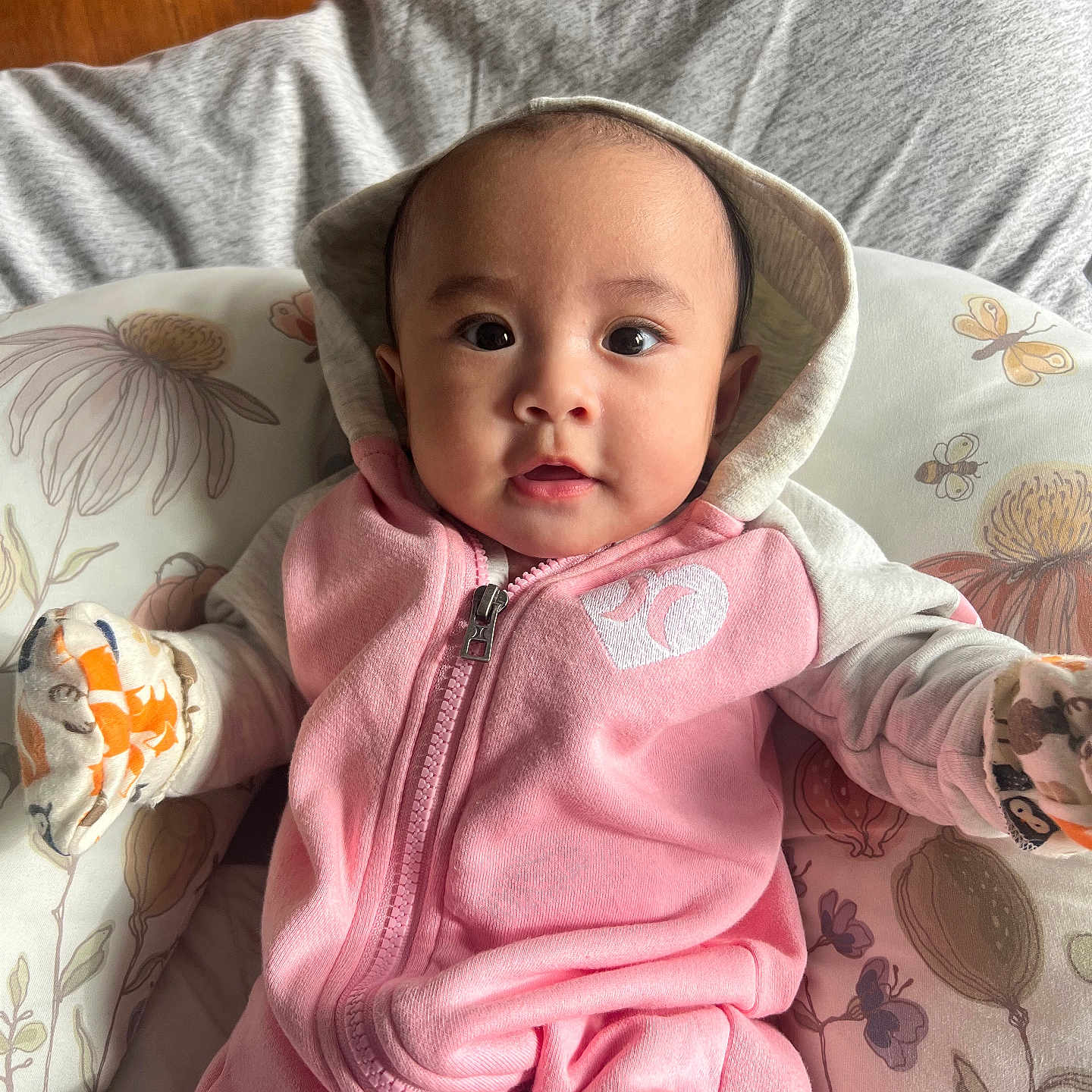 Zoey joined the competition — help win amazing prizes! apparel, baby, baby_clothes, child, comfort, cozy, cushion, cute, expression, face, floral_pattern, hoodie, indoors, infant, mittens, person, pink_clothing, portrait, seated, young_child