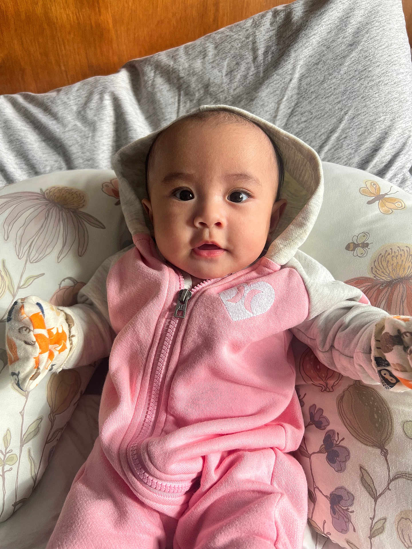 Zoey joined the competition — help win amazing prizes! baby, infant, hoodie, pink_clothing, mittens, cushion, floral_pattern, face, portrait, child, cute, indoors, comfort, young_child, apparel, seated, expression, person, baby_clothes, cozy