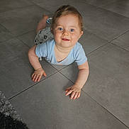 Timéo a rejoint le concours — aidez-le/la à gagner de superbes lots ! baby, child, crawling, blue_shirt, tiled_floor, rug, living_room, plant, furniture, smiling, happy, indoor, face, person, cute, young_child, floor, home, modern, curly_hair