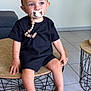 Soan participe au concours pour gagner de l'argent avec cette photo : toddler, child, pacifier, black_clothing, table, wooden_table, round_table, wireframe_table, indoor, tile_floor, footwear, sandals, bracelet, neutral_background, curious_expression, seated, shorts, short_sleeve, minimalist, baby