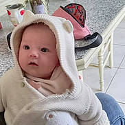 Emmy participe au concours pour gagner de l'argent avec cette photo : baby, hoodie, white_clothing, bear_patch, infant, kitchen, table, mug, face_mask, person, hand, jeans, red_toaster, cupboard, tile_floor, cozy, indoor, seated, cute, warm_lighting