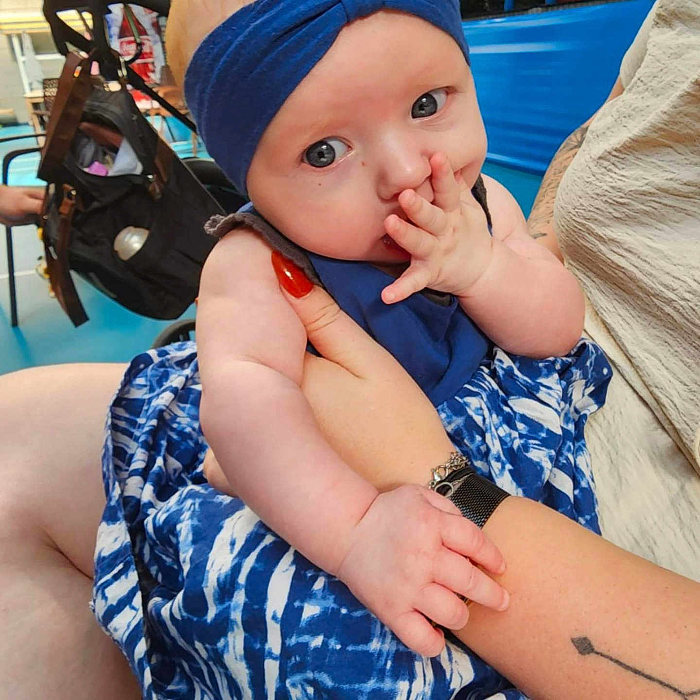 Agathe participe au concours pour gagner de l'argent avec cette photo : arm, baby, blue_dress, blue_headband, casual, child, clothing, cute, eyes, face, finger_sucking, flooring, hand, holding, indoor, person, seated, skin, stroller, tattoo
