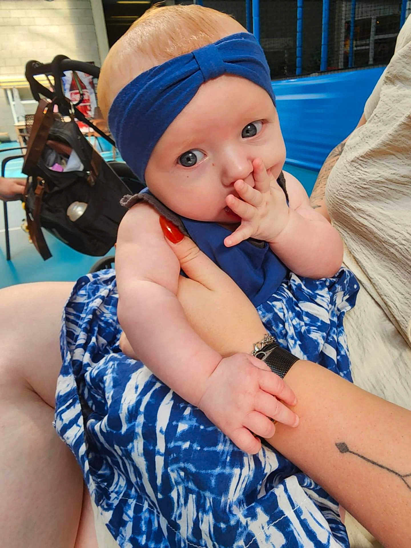 Agathe participe au concours pour gagner de l'argent avec cette photo : baby, child, blue_headband, blue_dress, finger_sucking, tattoo, arm, hand, person, indoor, stroller, flooring, casual, skin, face, eyes, clothing, holding, seated, cute