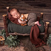 Eliott a rejoint le concours — aidez-le/la à gagner de superbes lots ! newborn, baby, sleeping, stuffed_animal, miniature_bed, wooden_bed, knit_blanket, brown_pants, lantern, pinecones, greenery, rustic, cozy, flooring, indoor, portrait, peaceful, infant, cute, soft_lighting