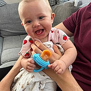 Hollie is registered to the contest to win money with this photo: baby, pacifier, adult, couch, blanket, clothing, face, hand, smile, tongue, infant, person, indoor, furniture, fabric, holding, pattern, happy, seated, skin