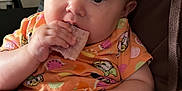 Hollie joined the competition — help win amazing prizes! baby, casual_clothing, child, closeup, comfort, curious_eyes, eating, face, hand, holding, indoor, infant, lap, orange_shirt, patterned_clothing, person, sitting, skin, snack, young_child