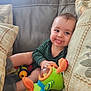 baby, child, tongue_out, smiling, plush_toy, cushion, sofa, striped_clothing, indoor, playful, cute, infant, sitting, happy, soft_toys, home, person, face, cozy, fun