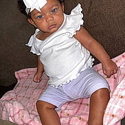 Armani joined the competition — help win amazing prizes! baby, child, curly_hair, blue_eyes, white_bow, headband, white_top, lilac_shorts, pink_blanket, plaid_blanket, couch, brown_couch, indoor, person, infant, cute, sitting, looking, soft_texture, relaxed
