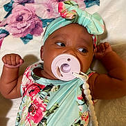 Deja joined the competition — help win amazing prizes! baby, infant, pacifier, headband, floral, dress, blanket, lying_down, child, cute, skin, hand, face, person, indoors, beads, accessory, looking, closeup, soft