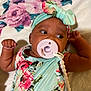 baby, infant, pacifier, headband, floral, dress, blanket, lying_down, child, cute, skin, hand, face, person, indoors, beads, accessory, looking, closeup, soft