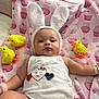 baby, bunny_ears, blanket, toy_chicks, pink, white_onesie, heart_design, bracelets, cute, infant, lying_down, soft_toys, plush, child, face, portrait, indoors, playful, adorable, soft_texture